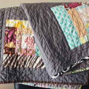 Stock image of a quilt with colorful accents and a dark grey background.